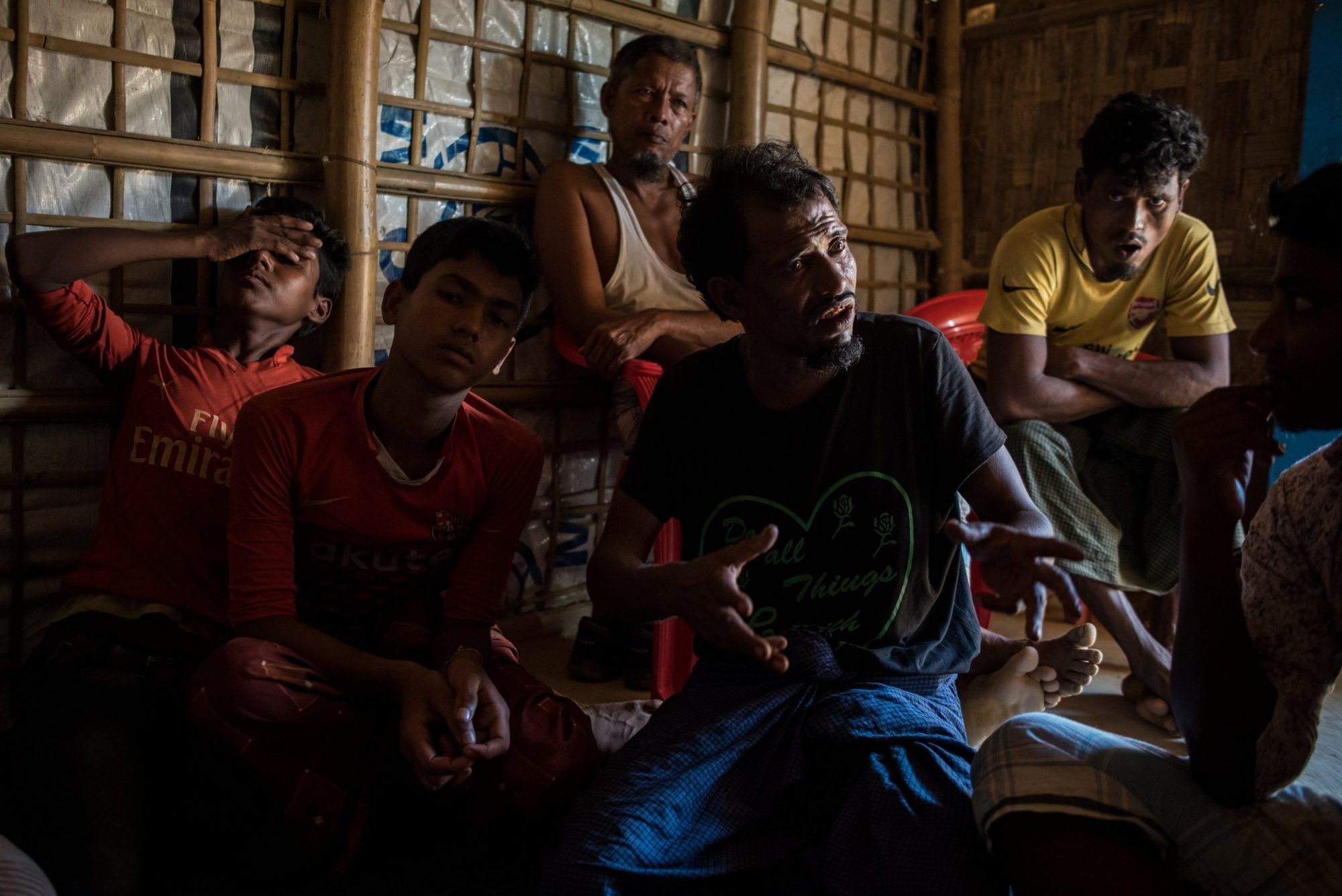 Men sitting and talking in a bamboo shelter, one with his hand over his face